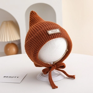 Detail of caramel knit baby pixie hat with pointed top and decorative miu tag