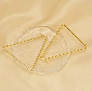 Detailed view of large gold triangular earrings on luxury gold satin background