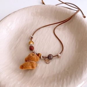 Detailed macro of a brown flocked puppy pendant necklace with beads on a ceramic tray