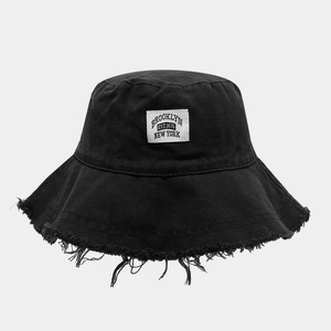 Détail des bords effilochés et de l'écusson Brooklyn sur un chapeau bob en toile noire