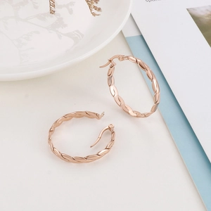Macro detail of rose gold twisted rope hoop earrings on a decorative white ceramic tray