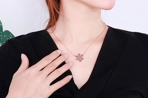 Close-up of a rose gold snowflake pendant necklace worn by a model on a black V-neck top