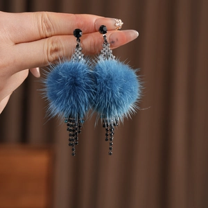 Detail view of long blue fur ball earrings with crystals and black metal tassels