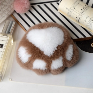 Detail of soft brown and white rex rabbit fur cat paw charm on striped background