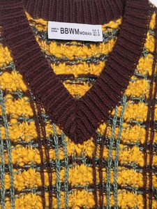 Macro shot of V-neck knit vest with yellow and brown textured plaid pattern and neck label