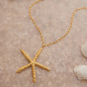 Gros plan d'un pendentif étoile de mer doré sur une chaîne sur un fond de plage de coquillages