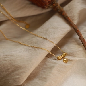 Macro shot of 18K gold plated bow and heart pendant necklace on textured fabric