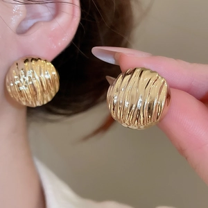 Detail showing the golden ripple texture on a circular earring worn on the earlobe