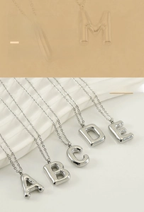 Macro detail of 3D bubble alphabet pendants in silver stainless steel on a textured base