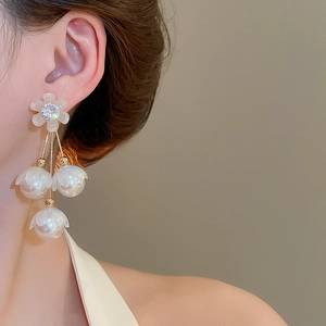 Gros plan de boucles d'oreilles fleurs dorées avec perles et zircons portées par un mannequin