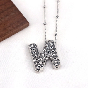 Macro shot of silver letter N pendant necklace with textured metal surface and bead chain