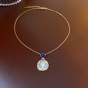 Detailed shot of retro gold necklace with blue gemstone and silver coin relief pendant