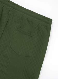 Detail of dark green tracksuit pants featuring quilted jacquard texture and elastic waistband