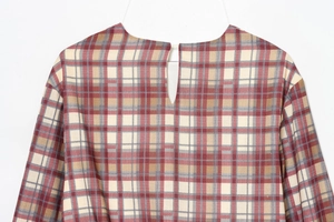 Dettaglio vestito a quadri rosso e beige con apertura a goccia posteriore e bottone