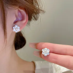 Detail of white camellia flower earrings with pearl center and golden edges on ear