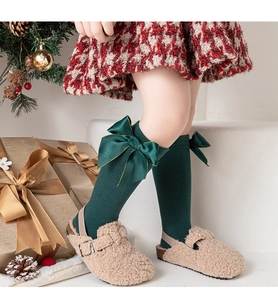 Détail de chaussettes en coton vert foncé avec gros nœud doré sur fond de fête