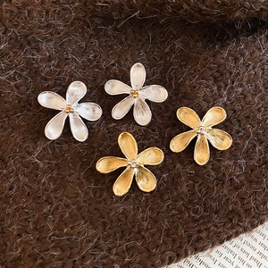 Dettaglio macro degli orecchini a fiore in metallo spazzolato argento e oro su tessuto
