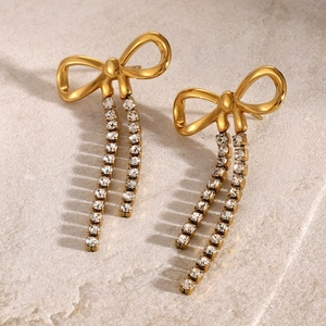 Macro shot of gold bow earrings featuring long rhinestone chains on a stone texture surface