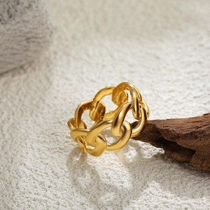 Detail of 18K gold chain ring displayed on a textured white surface with wood accent