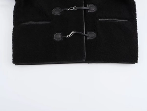Détail du manteau en peluche noir avec fermoirs en métal et bordures en similicuir élégantes