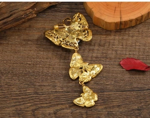 Detailed back view of golden butterfly brooch with pin and pendant loop on wood
