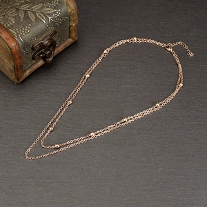 Detail of rose gold double-layered beaded necklace on a textured stone surface