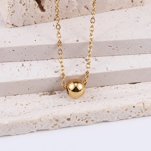 Macro shot of 18K gold ball pendant on a fine cross chain against a stone background