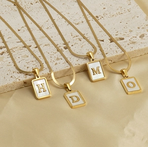 Detailed shot of four gold necklaces with rectangular shell letter pendants H, D, M, O