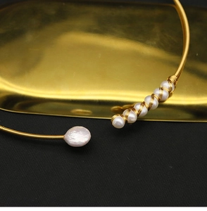 Macro shot of minimalist gold wire choker featuring natural white pearls and baroque pearl