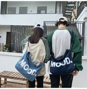 Detail of light and dark blue denim crossbody bags with MOOD print on a street background