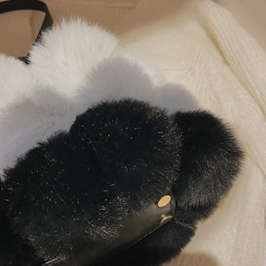 Close-up of fluffy black, white, and grey faux fur pom-poms with metal rivets on bag