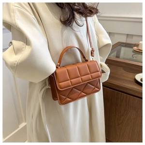 Brown quilted crossbody bag with gold hardware worn over a beige coat in a cafe