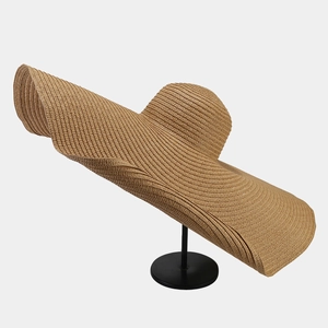 Detail showing oversized wavy brim straw hat on display stand with natural texture