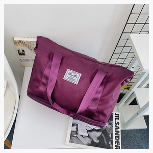 Detail of a large purple nylon travel bag with dual handles and woven logo patch