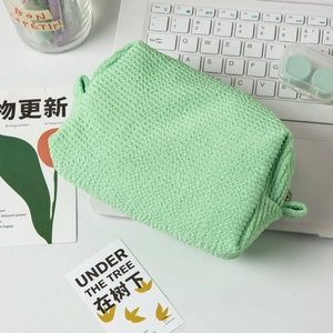 Detail of light green bubble-textured cosmetic bag with handle on a lifestyle desk setup