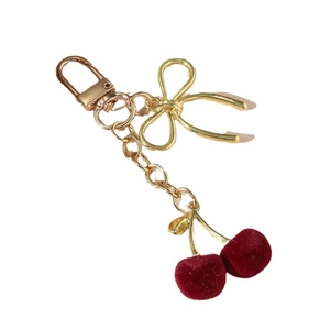 Shiny dark red velvet cherry keychain with golden bow accessory on white background