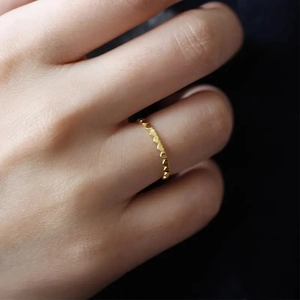 Close-up of minimalist gold ring featuring small connected heart elements on finger
