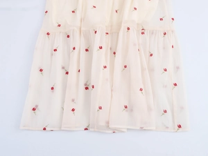Detailed macro view of the cream chiffon skirt hem featuring red floral rose embroidery