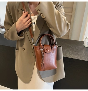 Brown leather bucket bag with woven charm shown cross-body on a khaki blazer