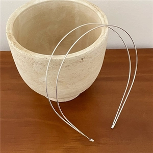 Close-up of a double-layered silver metal headband leaning against a white ceramic vase