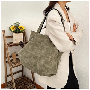 Olive green tote bag worn over shoulder, showing its large capacity and retro texture