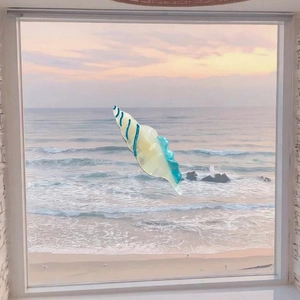 Close-up of a blue and cream striped conch shell hair clip against a sunset beach backdrop