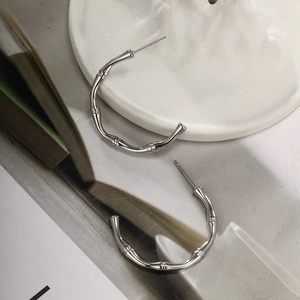 Macro view of C-shaped bamboo texture silver steel earrings on a minimalist white tray