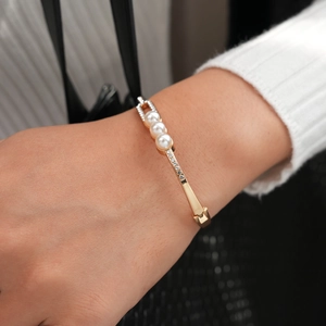 Close-up of gold-plated bangle with three pearls and crystal accents on a woman's wrist