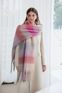 Close-up of a thick warm plaid scarf with tassels styled as a shawl over a beige coat