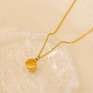 Close-up of 18K gold plated stainless steel necklace with round pendant on glass tray