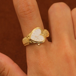 Macro shot of vintage gold heart watch ring featuring a textured band and white dial