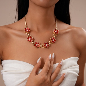 Close-up of a model wearing a gold chain necklace with red rhinestone flower charms