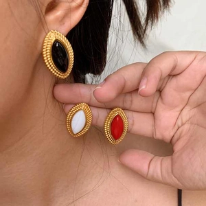 Macro detail of oval gold-plated earrings with black, white, and red stone inlays