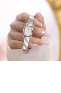 Detail view of square silver watch dial with Roman numerals and steel stretch band